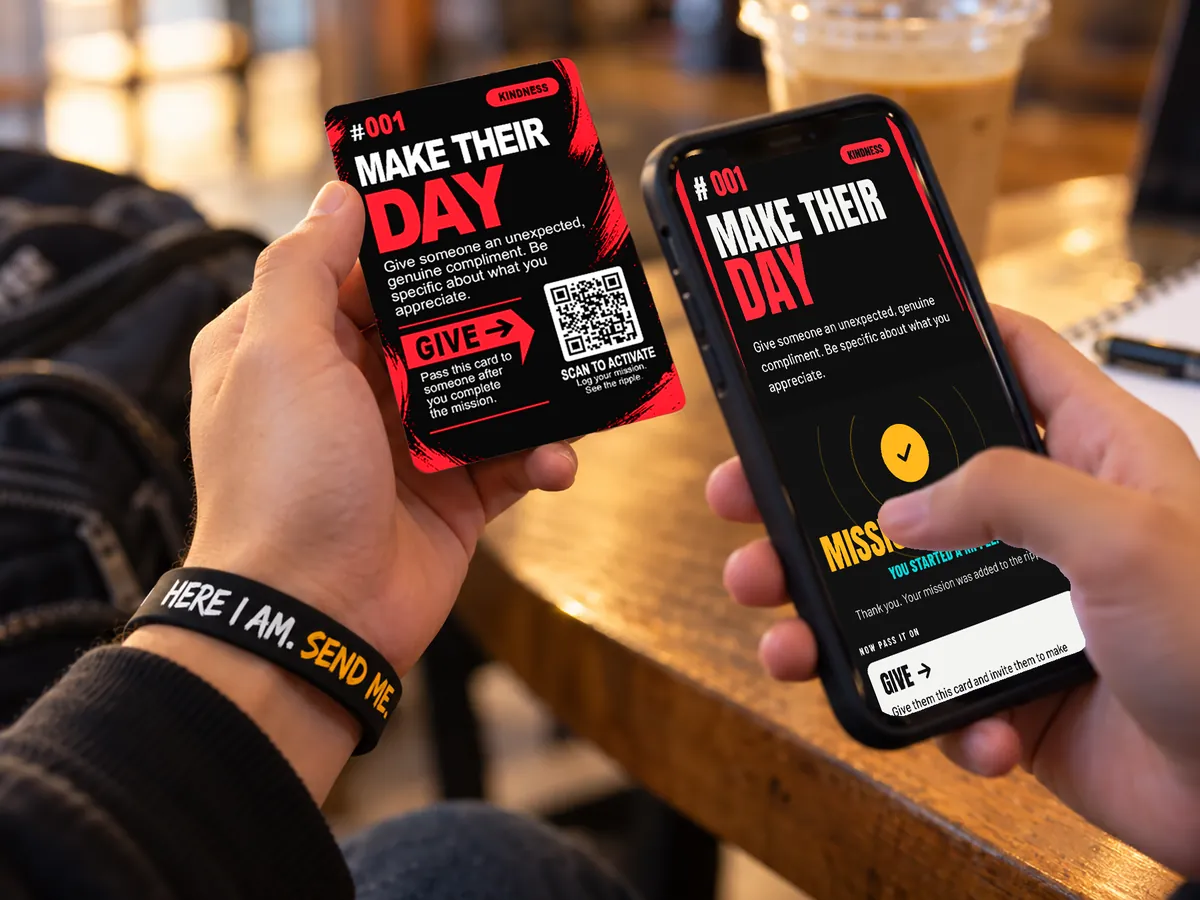 A hand holding mission card #001, Make Their Day, next to a phone showing the same mission on the ACT1V8 site, with the wristband on the wrist.